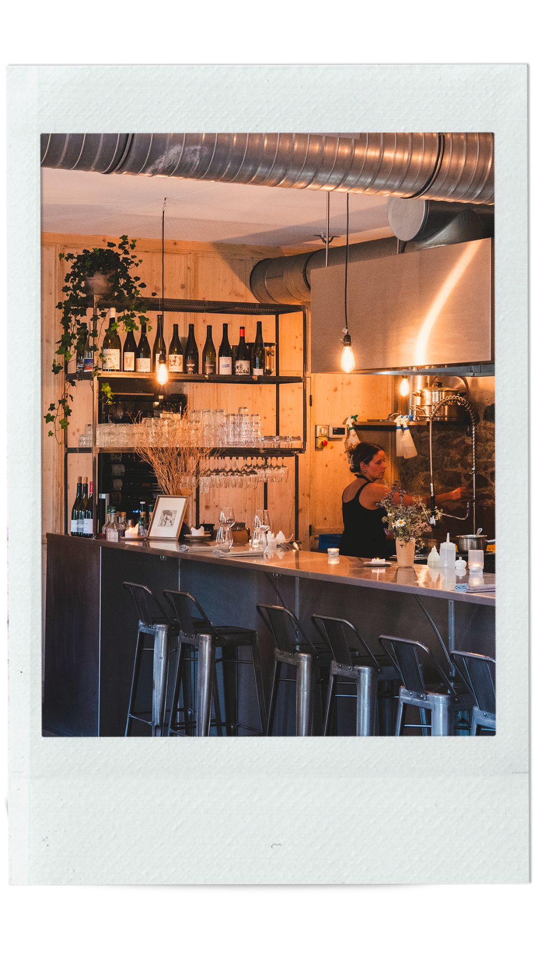 Étagère sur mesure de cuisine de restaurant vue dans son ensemble avec des bouteilles de vin, des verres et des plantes.