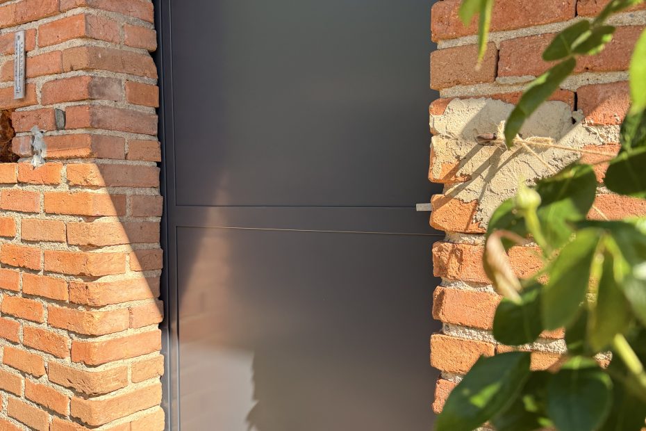Porte d'atelier en acier, l'entrée avec avec des briques et également un Rossier au primier plan.