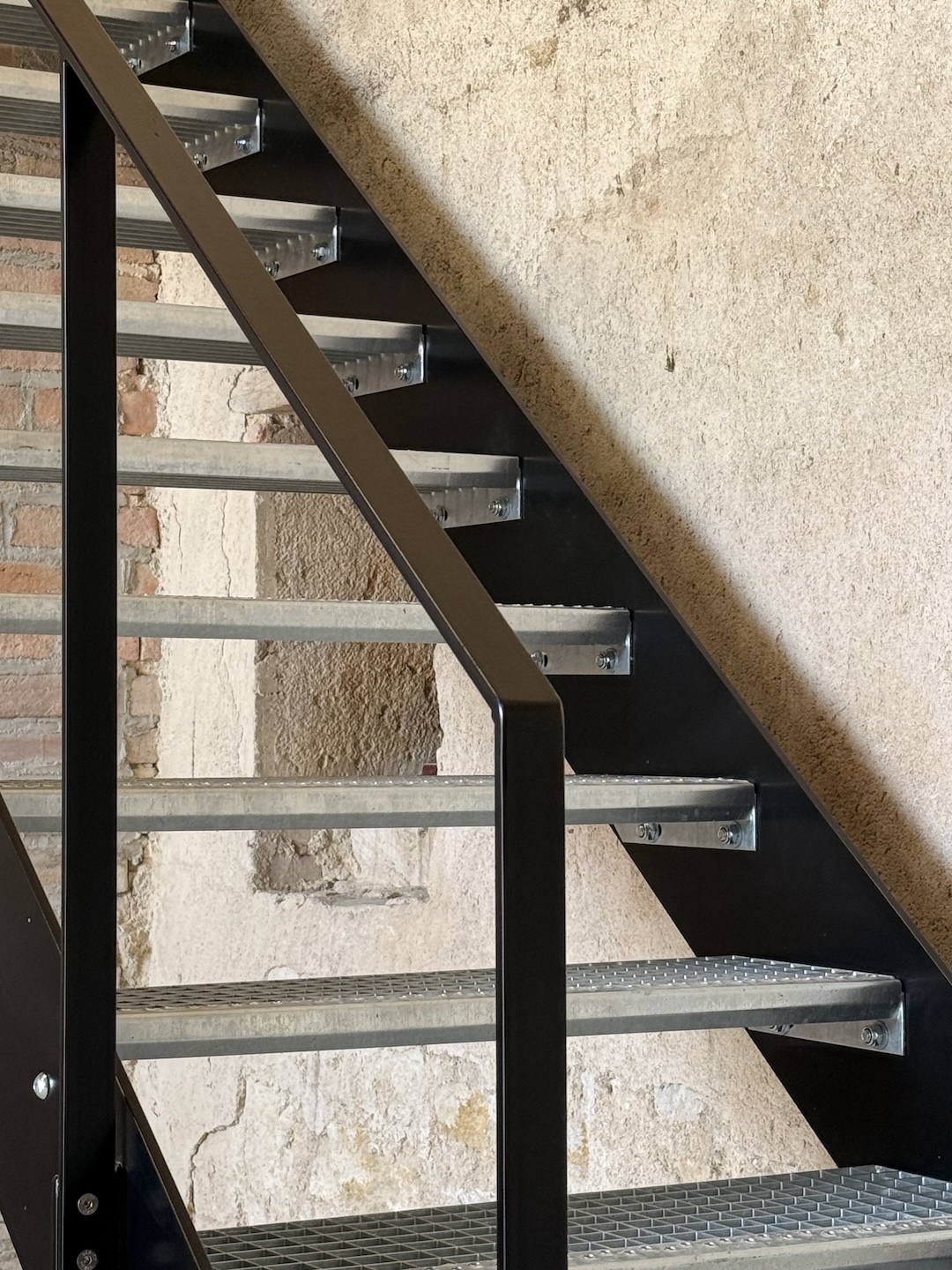 Détail d'une main courante d'un escalier en métal peint noir et marches galvanisées à chaud