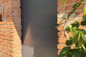 Porte d'atelier en acier, l'entrée avec avec des briques et également un Rossier au primier plan.
