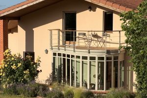 Verrière d'entrée en acier et garde-corps sur terrasse (vue de long) avec massif de fleurs sur le devant